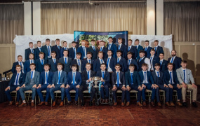Fitzgibbon Cup team and management posing with the cup at the Homecoming. There are three rows of 15 people, all wearing suits.