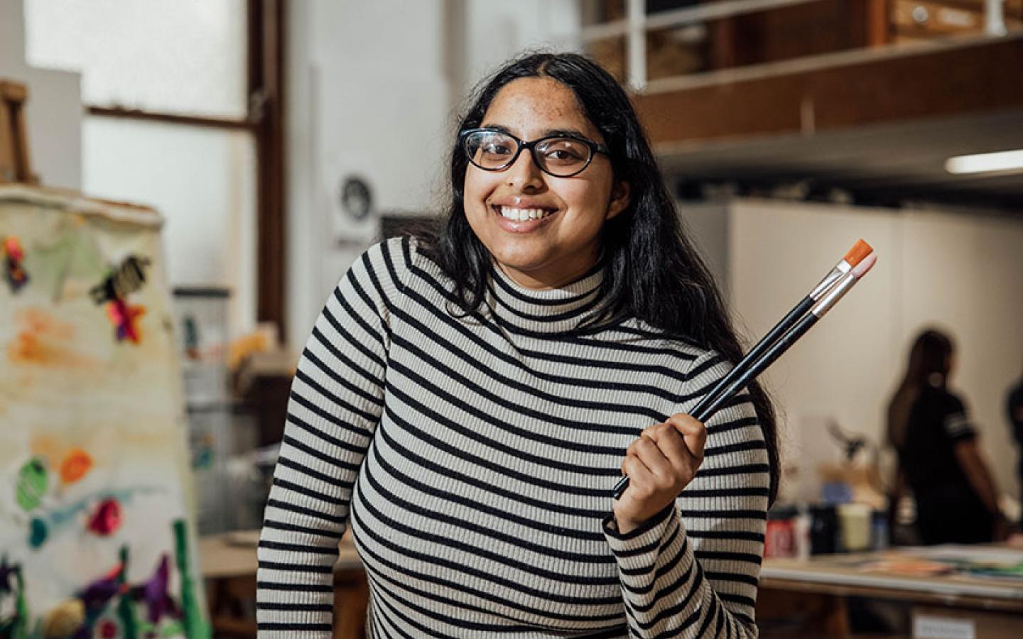 Student in art room holding paint brushes