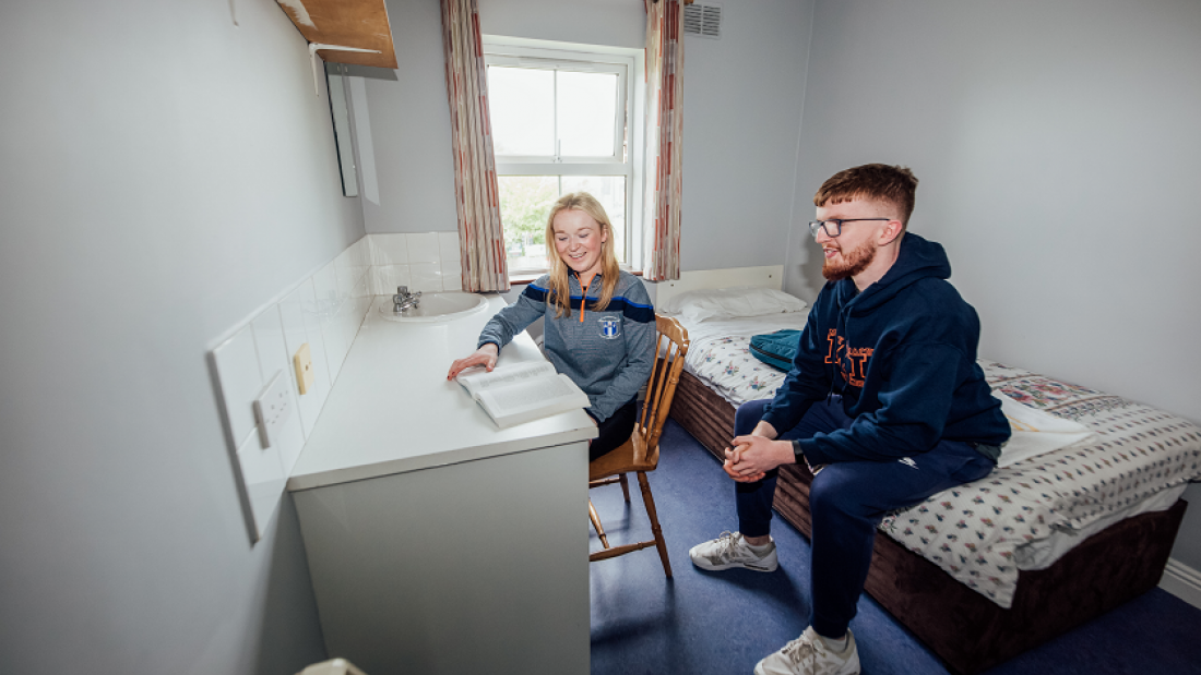 A female student and male student pictured in a bedroom with a desk and bed.