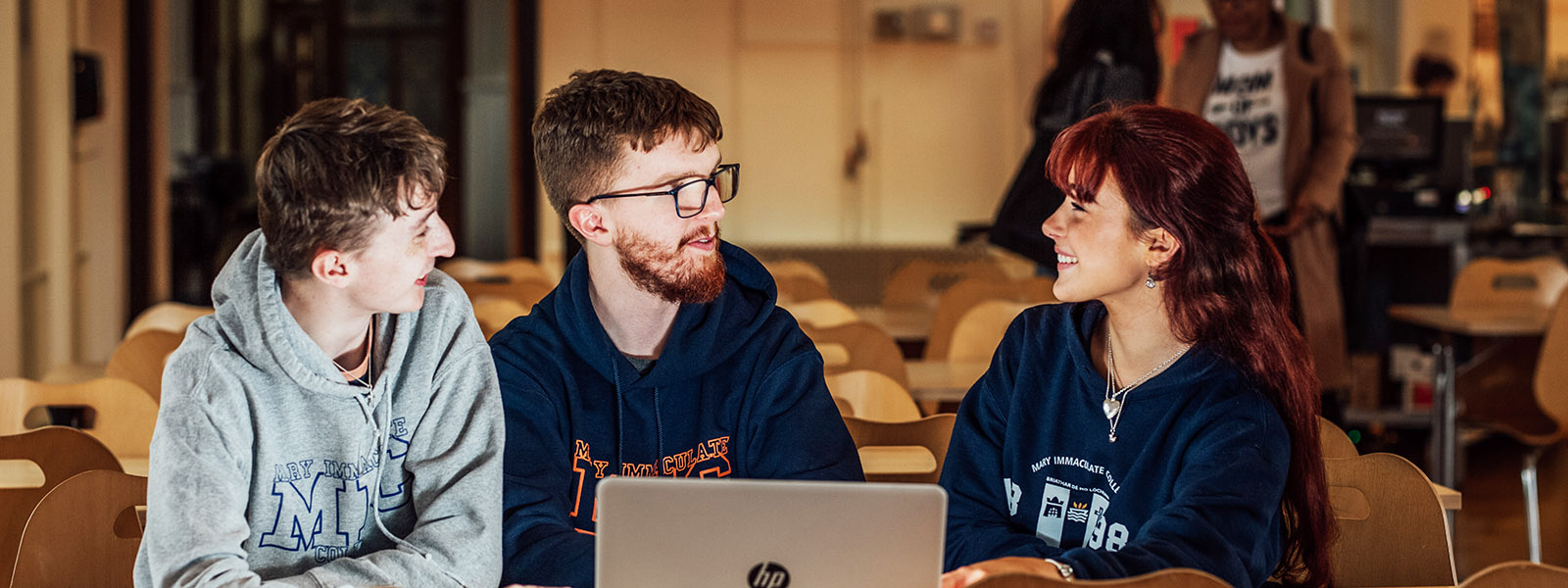 Female and two male students sitting at laptop talking.