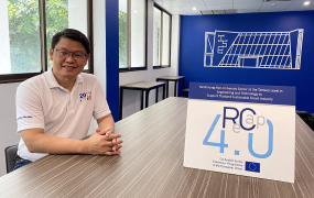 Project leader Dr Pisut Koomsap pictured in a board room in the Asian Institute of Technology. Dr Koomsap is pictured sitting with his hands on a table. Also on the table is a sign saying ReCap 4.0