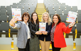 Four females posing for a photo holding up a leaflet for the Lifelong Learning Festival