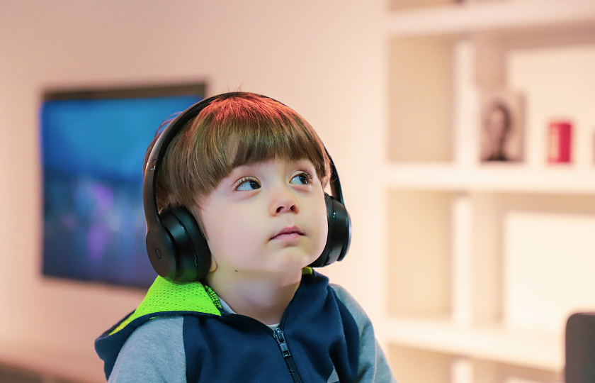 An autistic child sits looking upwards while wearing noise cancelling headphones