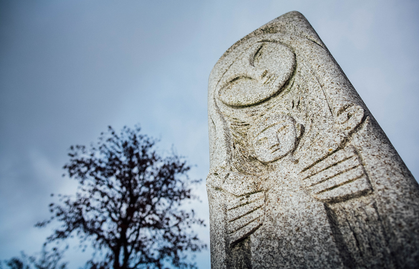 An Imogen Heap sculpture of the Virgin Mary stands beside a tree without leaves against a grey sky