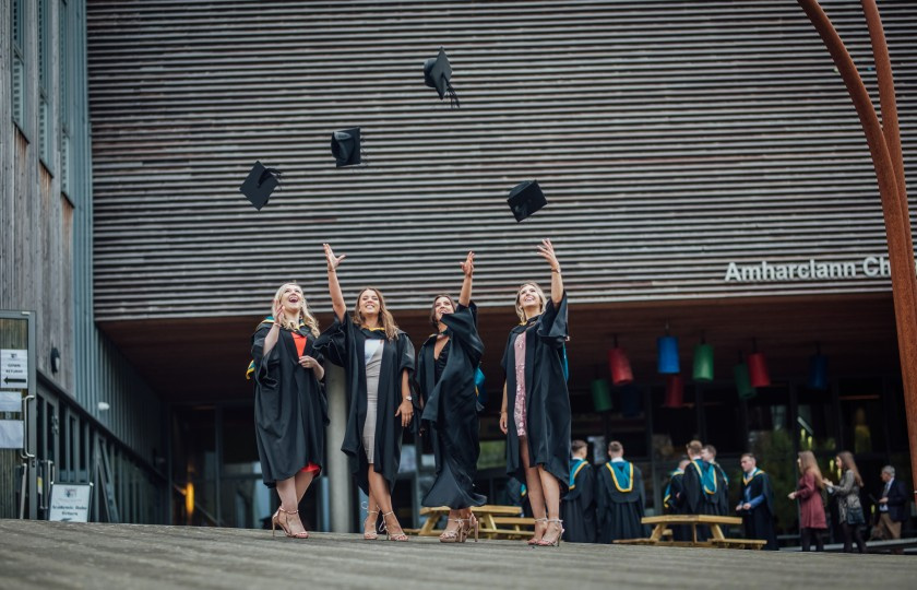 Four MIC students throw their hats into the air