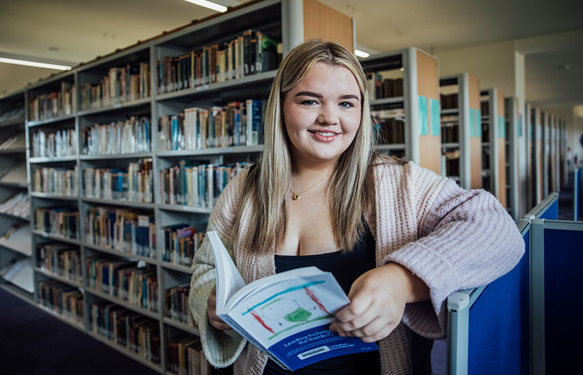 Female student holding an open book in the library