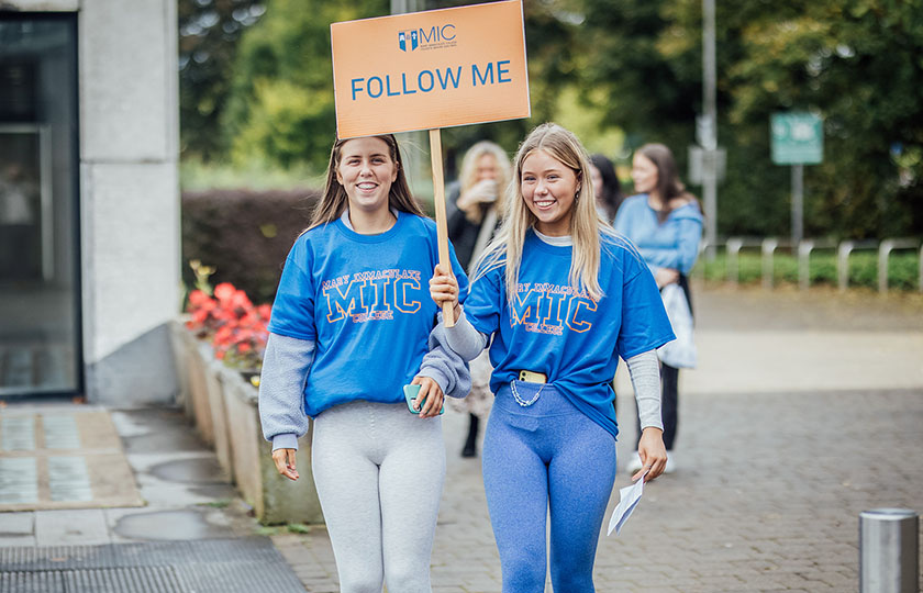 Two students carrying a Follow Me sign on open day