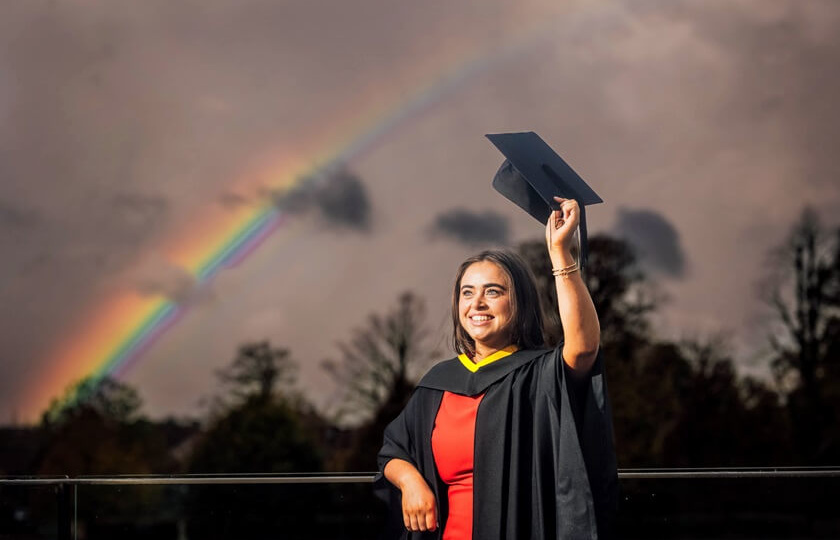 female graduate in cap and gown with rainbow at MIC Graduation 2024