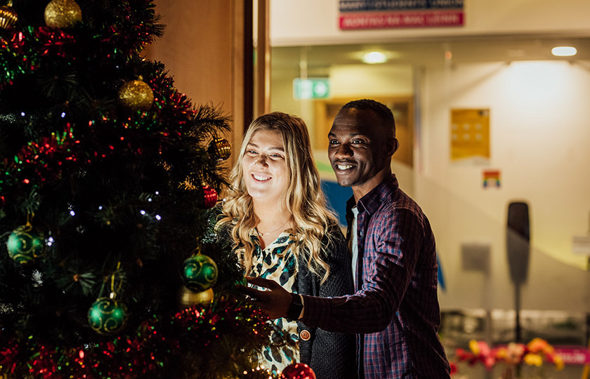 Two postgraduate students looking at the Christmas tree.