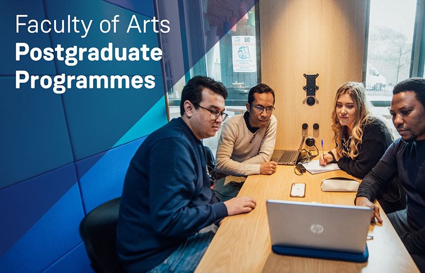 Four postgraduate students sitting at a table looking at a laptop