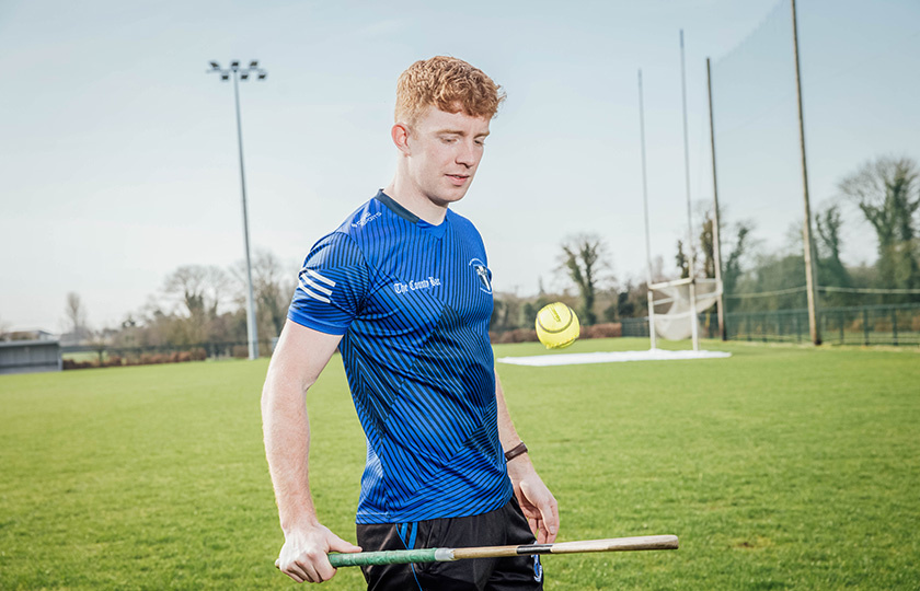 A student practicing hurling on the college field.