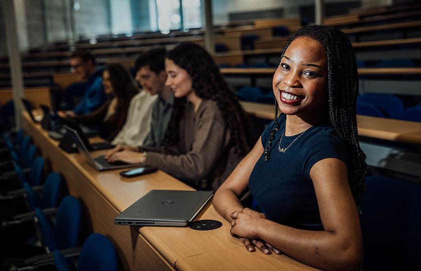 Student looking at camera, sitting in a lecture theatre with other students