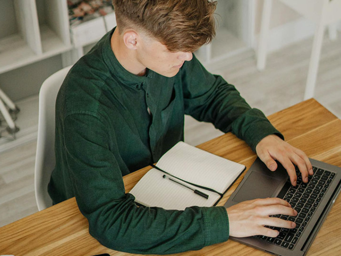 Man sitting at a desk with a laptop and notebook