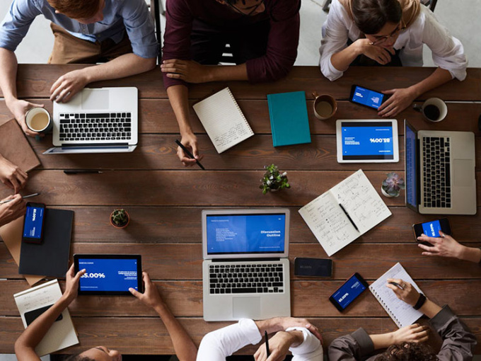 Eight people sitting around a table with laptops and notebooks.